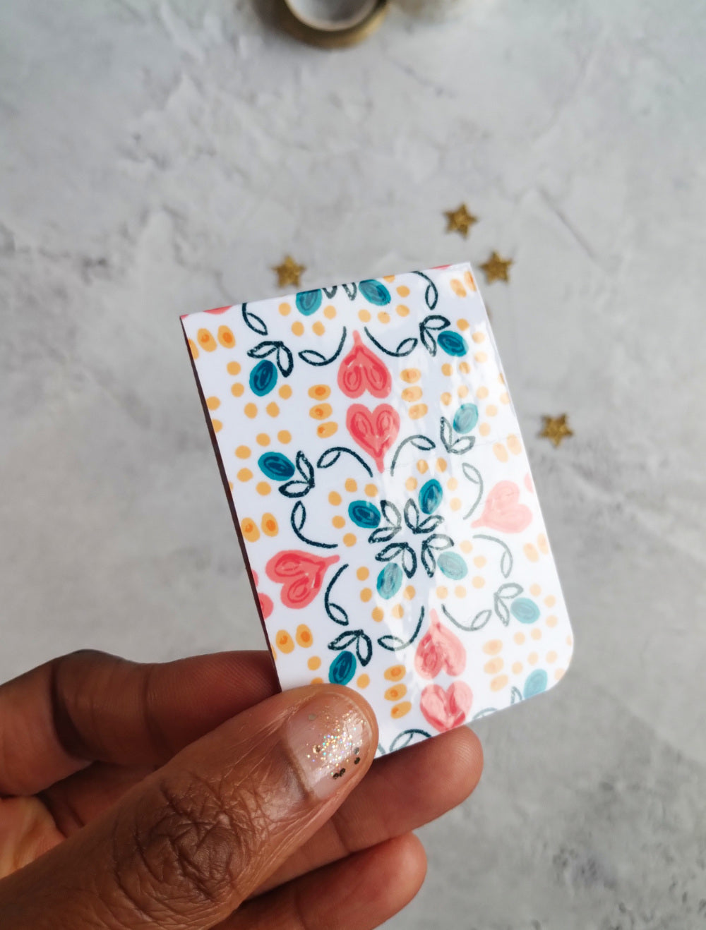 Hand holding glossy Summa Love Magnetic bookmark with bright heart pattern design.