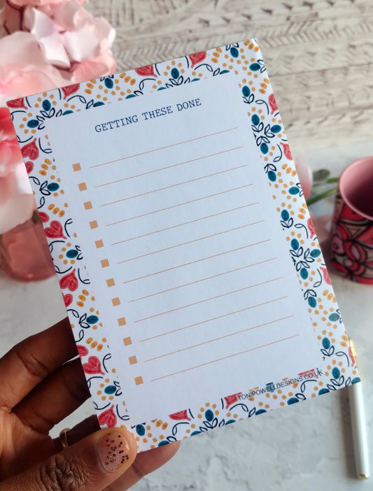 A6 Notepad with a heart pattern decorative border held by a hand, with a blurred background