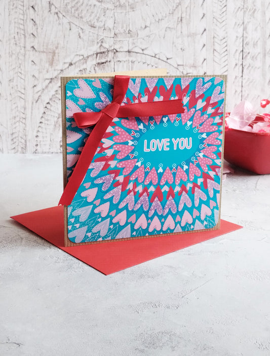 Teal Love radiating hearts greeting card with a hand tied red ribbon and red envelope