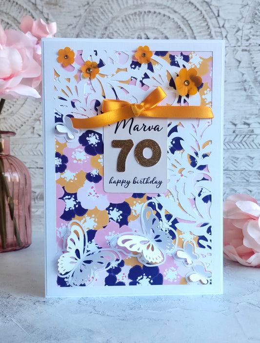 Birthday card with floral design, yellow ribbon, and '70 happy birthday' tag on a light background.