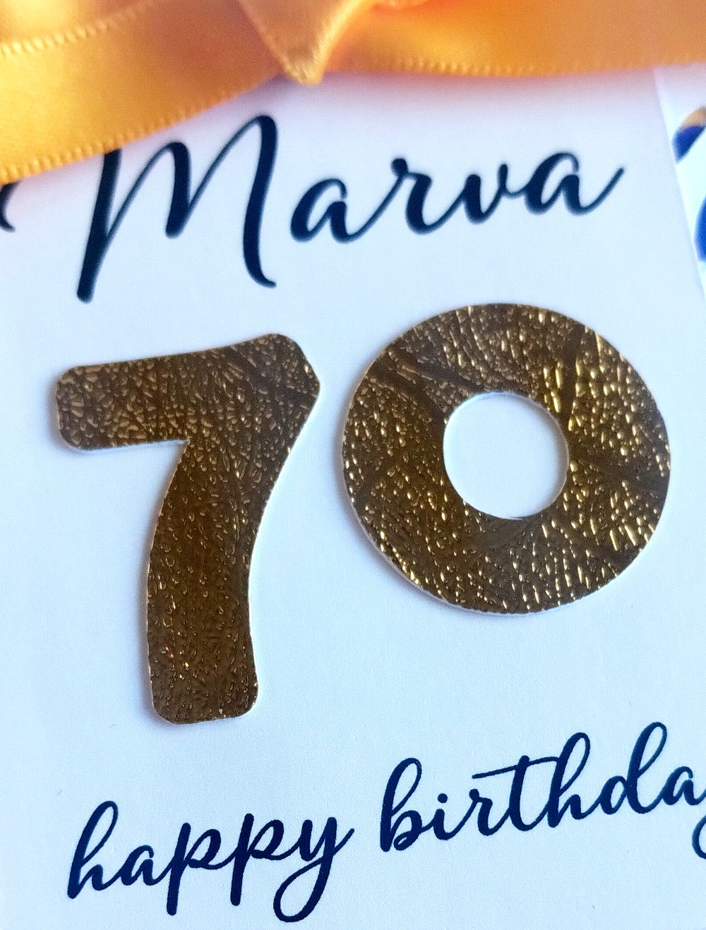 Gold number '70' on a white card with blue text and a gold ribbon.