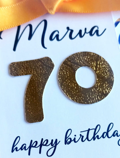 Gold number '70' on a white card with blue text and a gold ribbon.