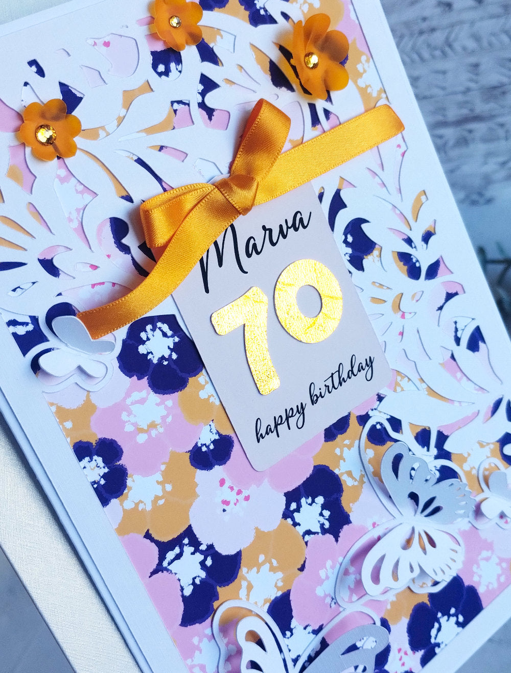 Birthday card with floral design, gold number 70, and yellow ribbon on a white background
