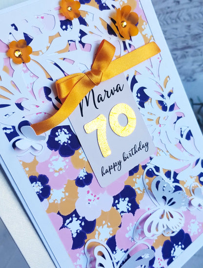 Birthday card with floral design, gold number 70, and yellow ribbon on a white background