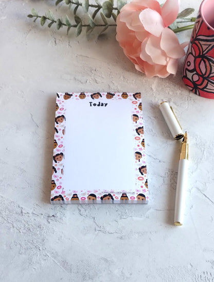 Notepad with cute faces, doughnuts, cupcakes and tea-cups design, on a white table with a pen ready to write.