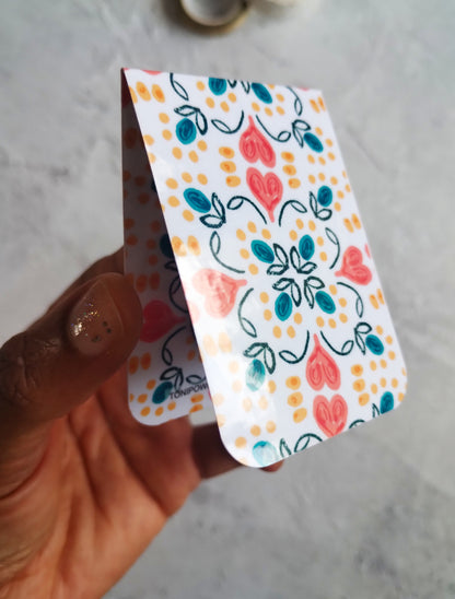 Hand holding a colourful, glossy Summa Love magnetic bookmark with heart pattern design