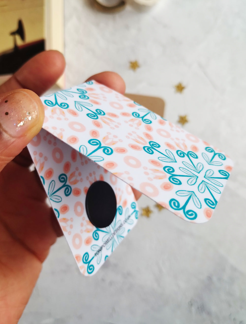 Hand holding an open Summa Tulip magnetic bookmark with a floral pattern.