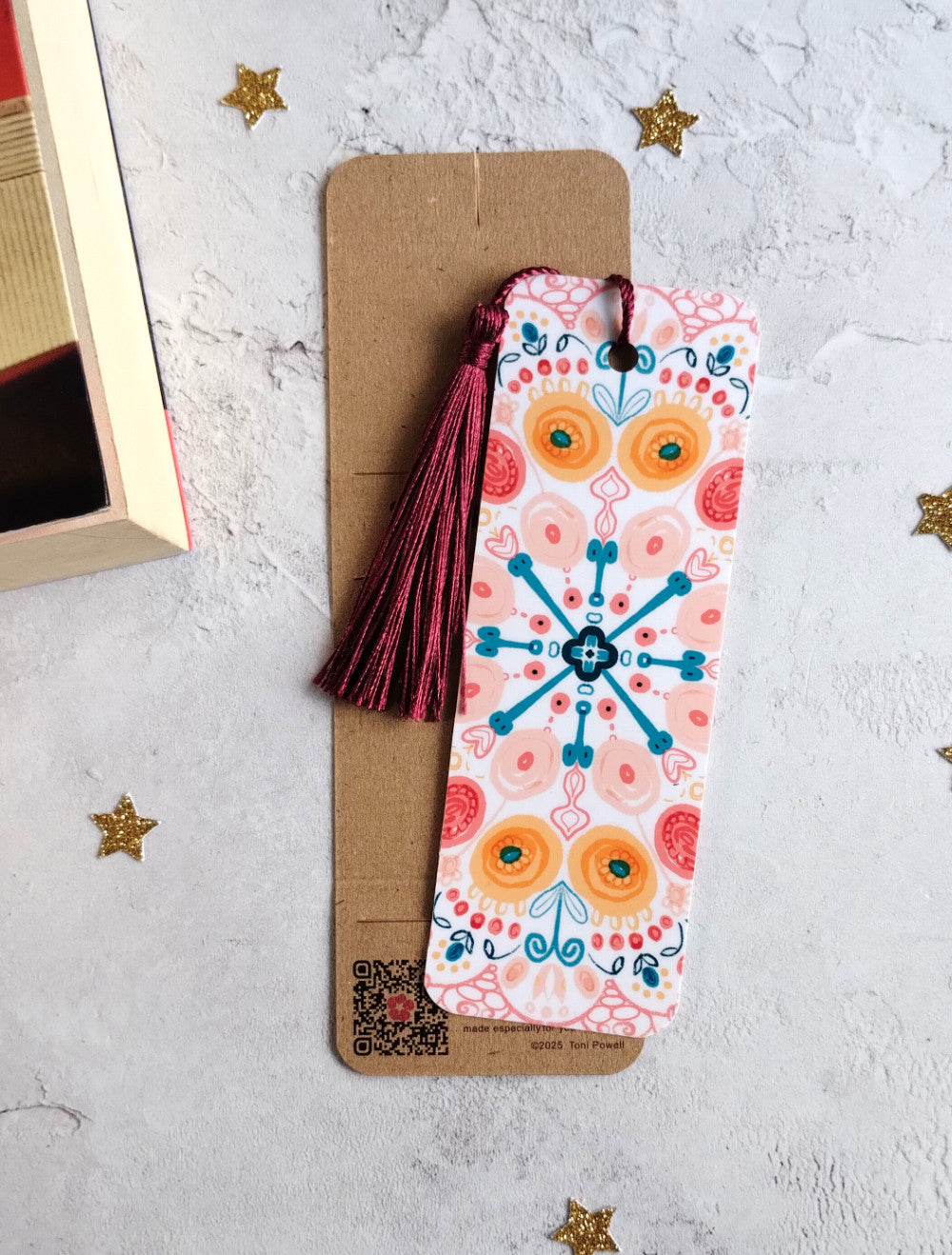 Summa Burst brightly patterned bookmark embellished with a beetroot red tassel, outside of packaging