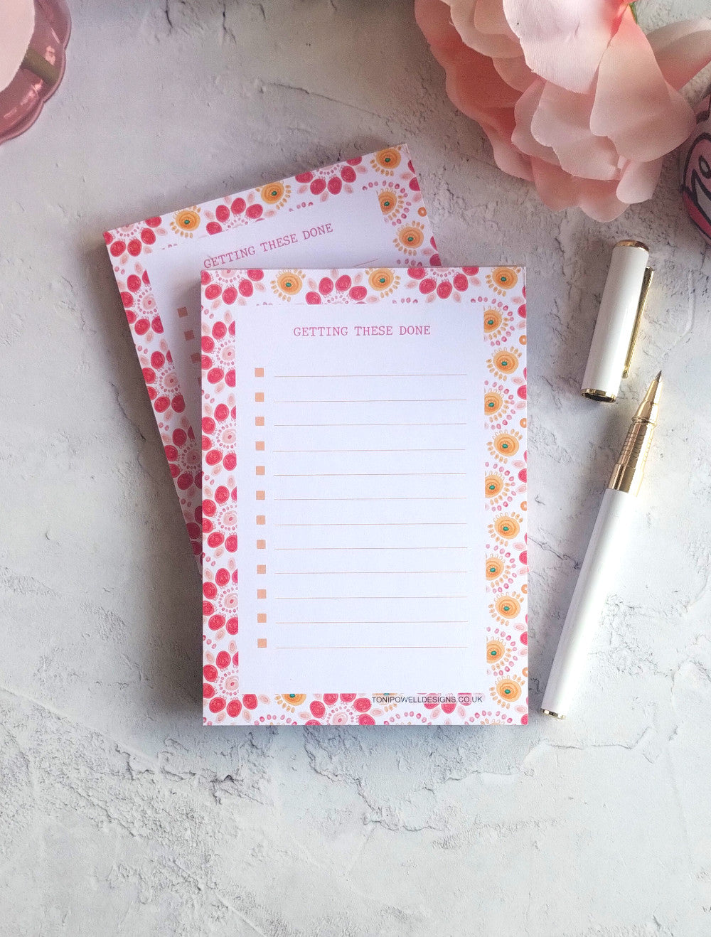 Two bright pattern notepads with a pen on a light surface