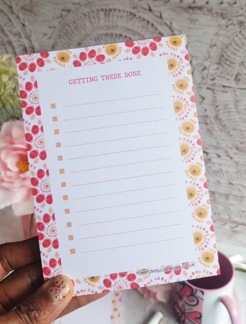 Notepad with a bright pattern border held by a hand, with text 'GETTING THESE DONE'.