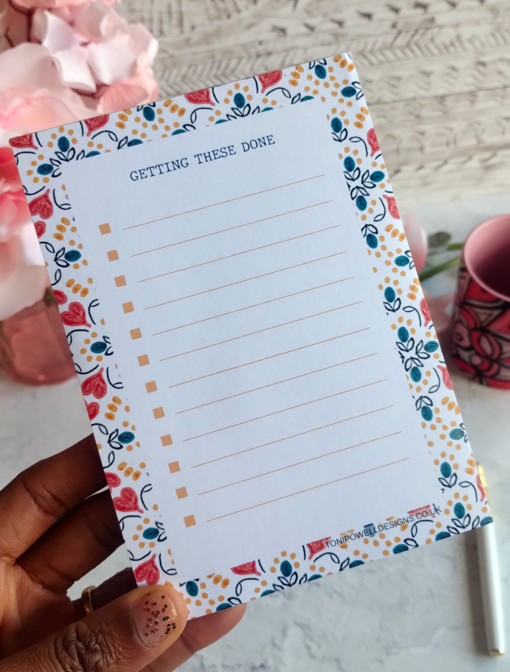 A6 Notepad with a heart pattern decorative border held by a hand, with a blurred background