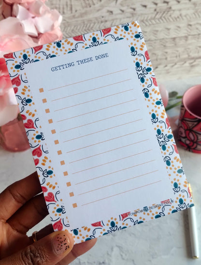 A6 Notepad with a heart pattern decorative border held by a hand, with a blurred background